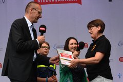 Auf der Radio-Bühne von Antenne Niedersachsen überreicht Bischof Thomas Adomeit eine Urkunde an Silvia Zahn-Claus aus Heppens. Sie wird als Heldin des Alltags ausgezeichnet. Foto: Axel Biewer