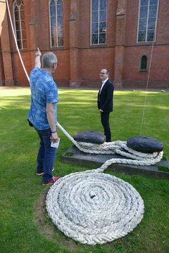 Pfarrer Frank Morgenstern (li.) erläutert dem Niedersächsischen Kultusminister Grant Hendrik Tonne die Kunstinstallation „Festmachen“ an der Christus- und Garnisonkirche. Die Kirche ist mit einem armdicken Tampen (Schiffstau zum Festmachen) an einem